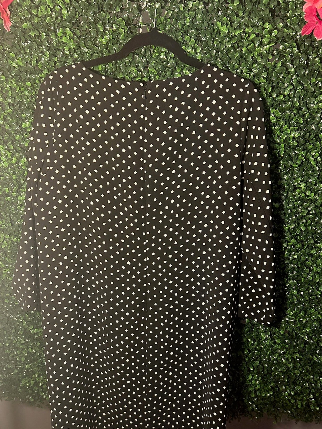 Black dress with white polka dots on a hanger against a green leafy background
