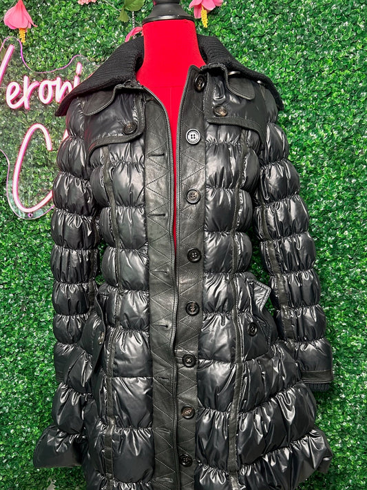 Black puffer coat on a mannequin against a green leafy background