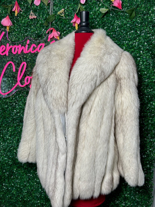 White fur coat on a mannequin against a green textured wall with pink floral decorations and 'Veronica' text.