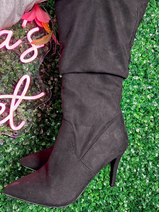 Black knee-high boot being held against a green grass background with a neon sign.